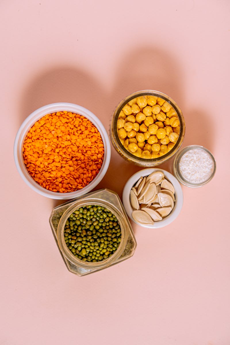 Variety of raw seeds and legumes on pink background for healthy cooking ideas.